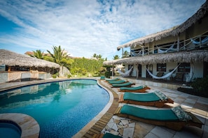 A pool area with lounge chairs and a thatched-roof building. - 7 Beaufort - Kitesurf Pousada (Itarema)