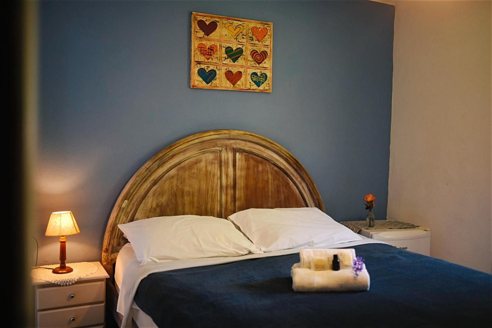 A bed with a wooden headboard, white bedding, a bedside lamp, and a small table with a vase of flowers.