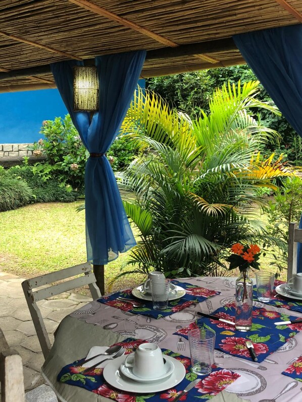 Un área de comedor al aire libre con una mesa dispuesta para dos personas, rodeada de exuberante vegetación y un techo de bambú.
