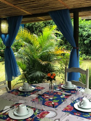 Un área de comedor al aire libre con una mesa dispuesta para dos personas, rodeada de exuberante vegetación.