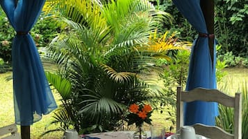 An outdoor dining area with a table set for two, surrounded by lush greenery.