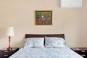 Quarto de hotel com cama, mesa de cabeceira, luminária, quadro e ar condicionado.