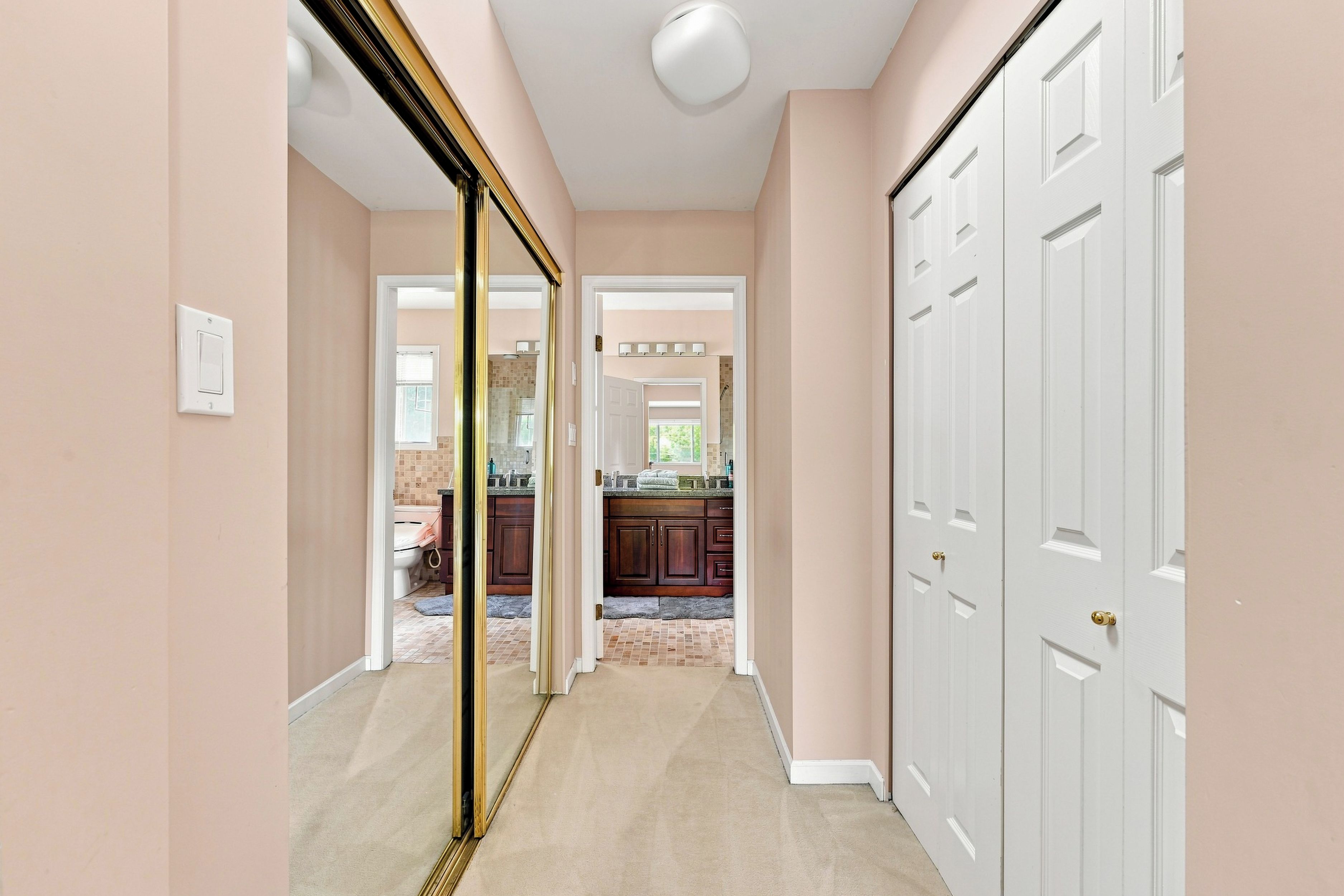 A hallway with a mirrored wall, a white door, and a kitchen area visible through an open door.