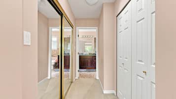 A hallway with a mirrored wall, a white door, and a kitchen area visible through an open door.