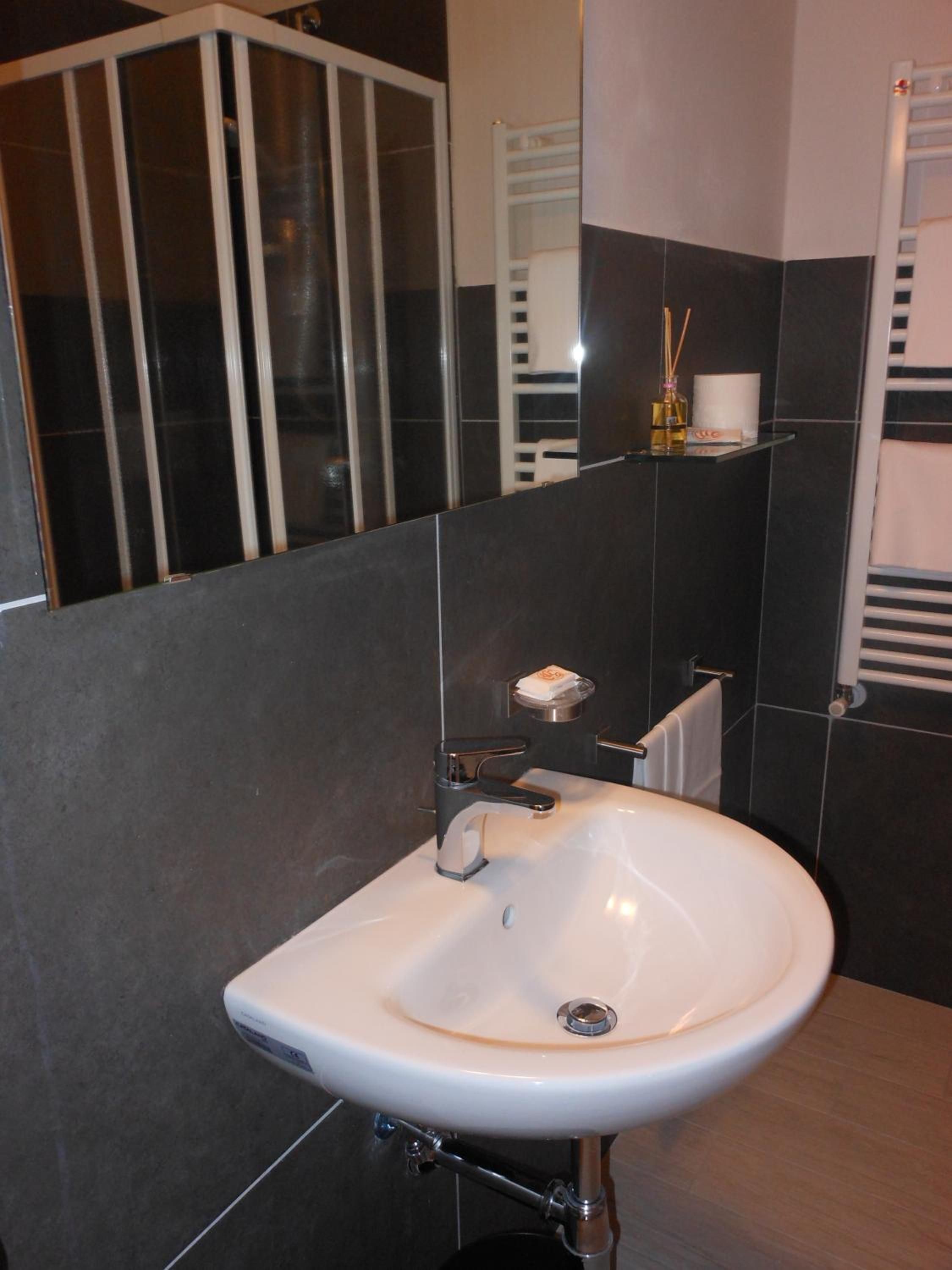 A bathroom with a white sink, dark tiled walls, a mirror, and a towel rack.