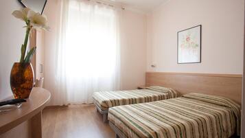 Una camera d'albergo con due letti, una scrivania, un vaso con fiori e un quadro appeso al muro.