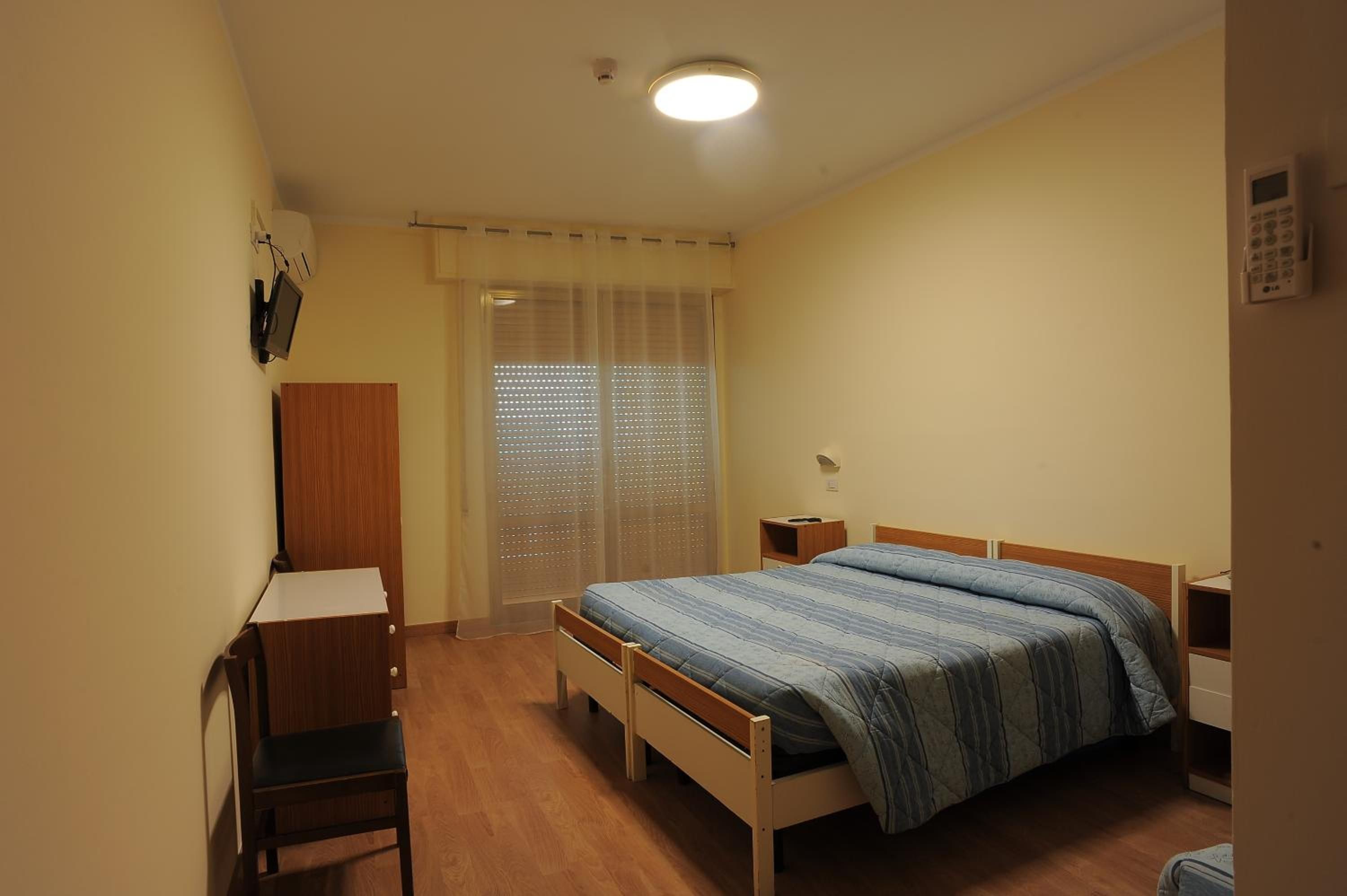 Una camera da letto con un letto, una scrivania, una sedia, un armadio e una finestra con persiane.