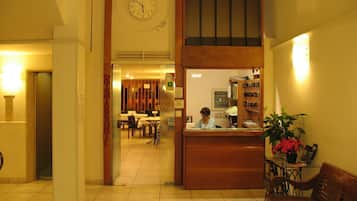Una hall d'albergo con una reception, un orologio, una sala da pranzo e una panca in legno.