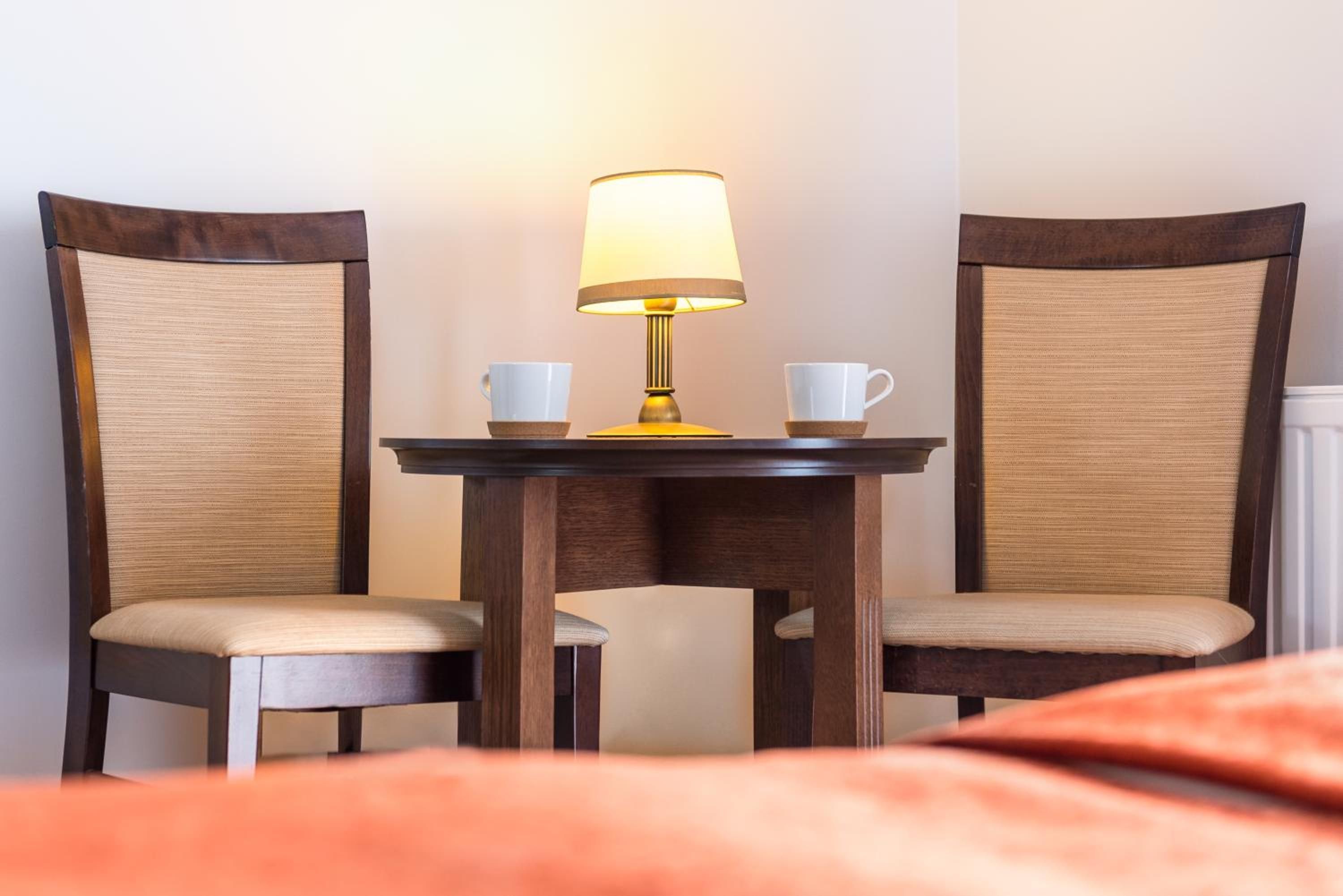 A hotel room with a bed, a table with two chairs, and a lamp.
