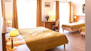 A hotel room with two beds, a desk, a chair, and a lamp.