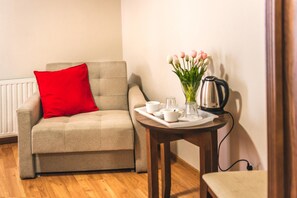 A cozy room with a beige sofa, a red pillow, a small table with a coffee pot, cups, and a vase of flowers. - Airpark Balice (Zabierzow)