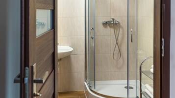 A modern bathroom with a glass-enclosed shower, a white sink, and wooden flooring.