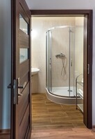 A modern bathroom with a glass-enclosed shower, a white sink, and wooden flooring.