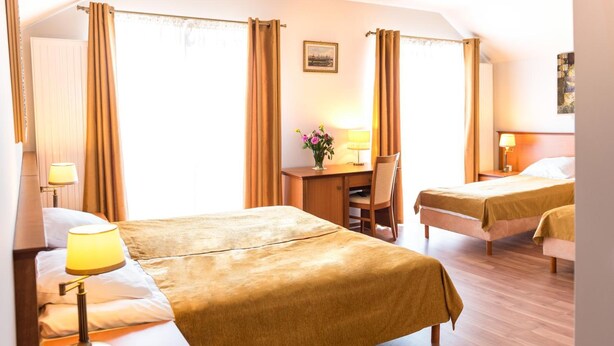 A hotel room with two beds, a desk, a chair, and a lamp.