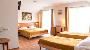 A hotel room with two beds, wooden flooring, a painting on the wall, and a window with curtains.