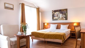 A hotel room with a bed, a sofa, a small table with a vase of flowers, and a painting on the wall.