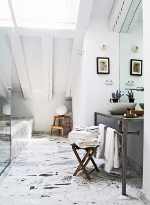 A modern bathroom with a glass shower enclosure, a wooden stool, a marble floor, and a sink with a basin.