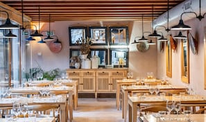 En restauranginteriör med flera matbord, stolar och hängande taklampor.