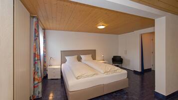 A bedroom with a wooden ceiling, a bed with white bedding, a nightstand with a lamp, and a chair.