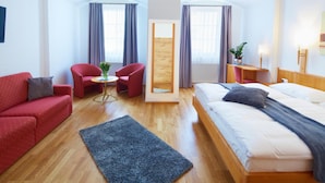 Una habitación de hotel con una cama, un sofá rojo, una mesita con un florero y un espejo.