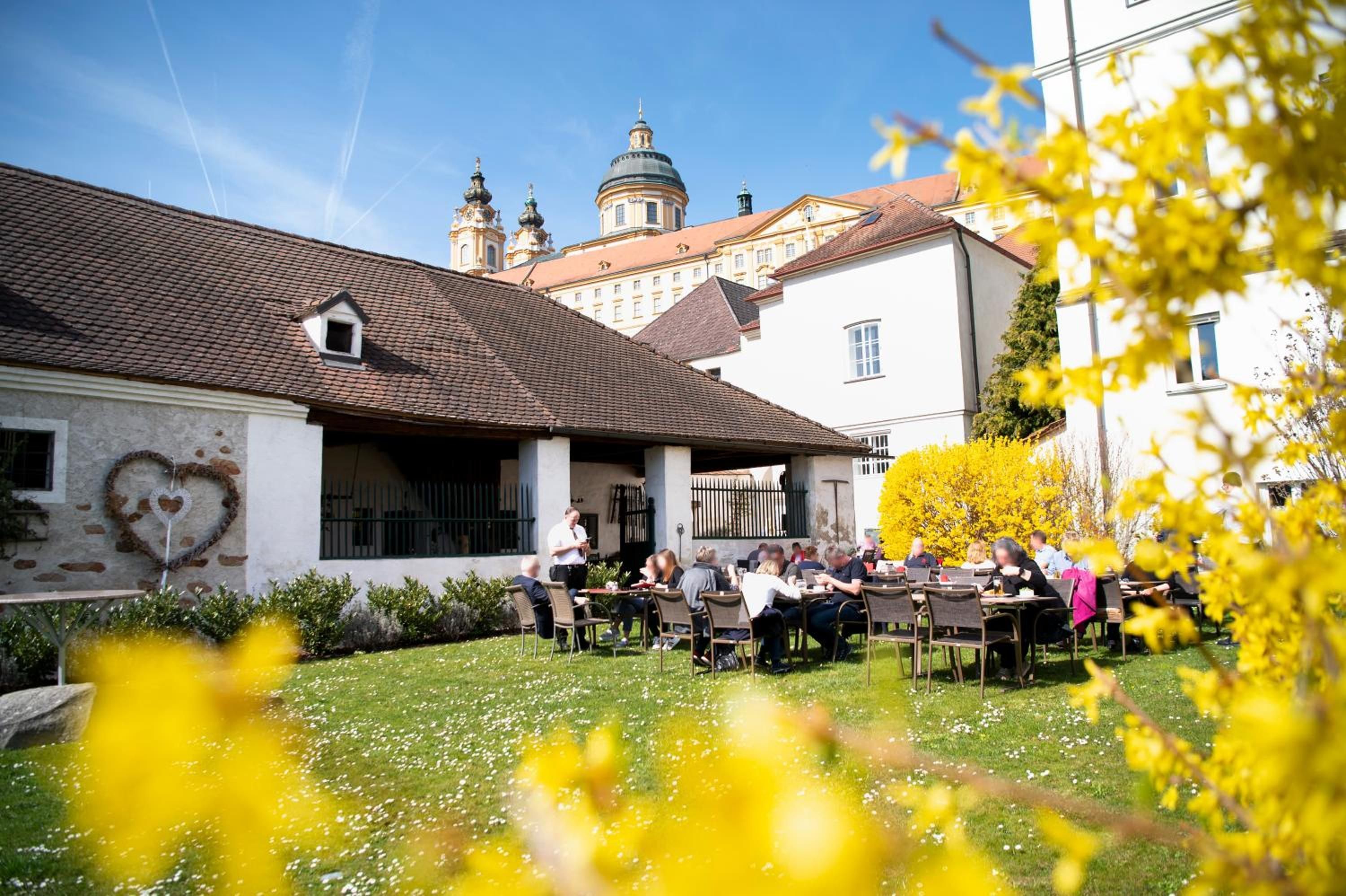 An outdoor seating area with tables and chairs, surrounded by a garden with yellow flowers.