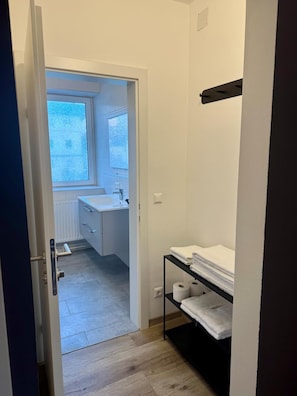 A narrow hallway leading to a bathroom with a window, a sink, and a shelf with towels. - Rathauskeller Melk (Melk)