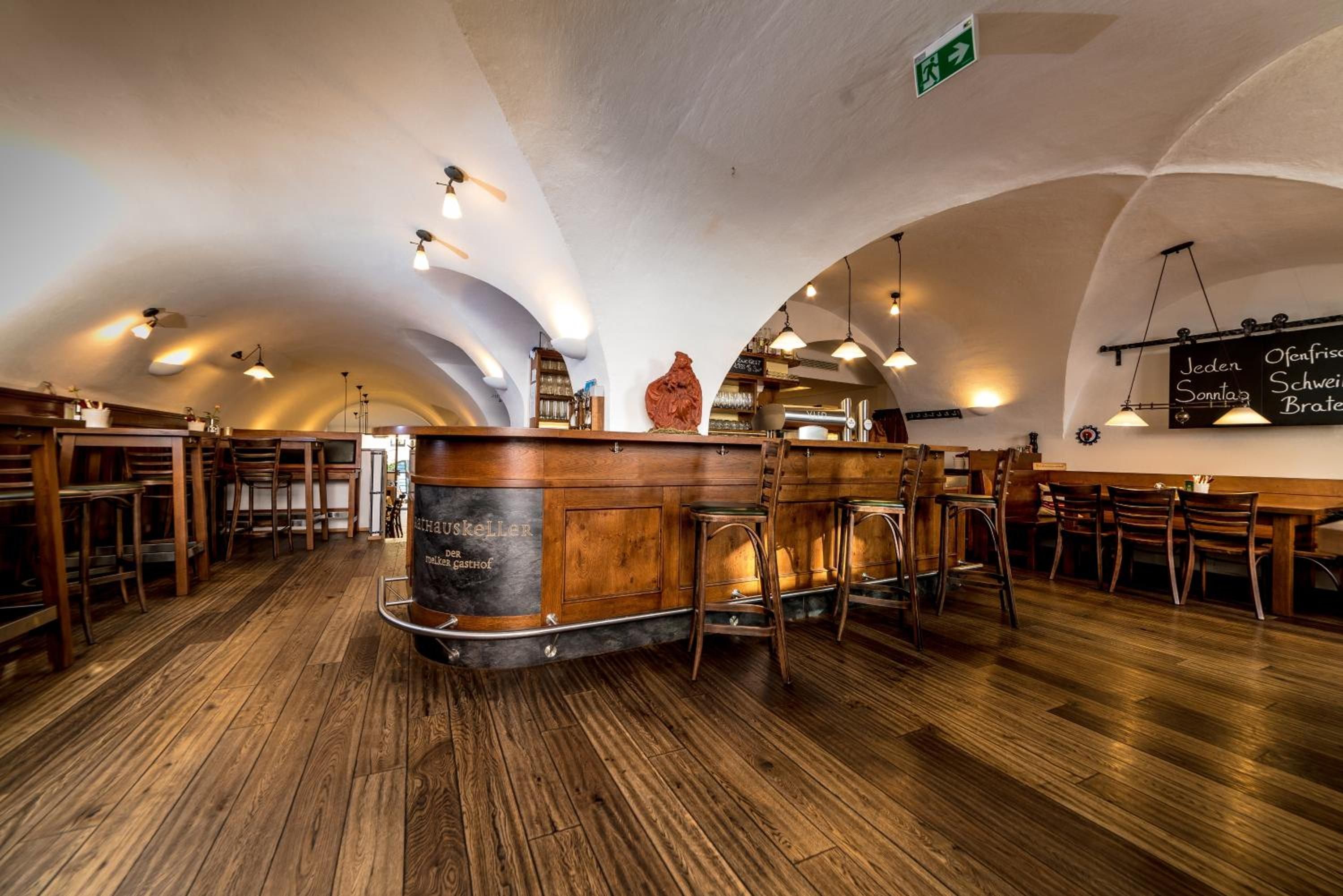A restaurant interior with wooden flooring, a central bar area, and arched ceiling.