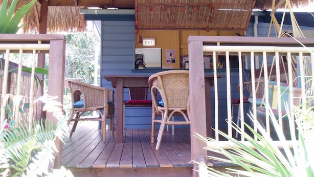 Un espacio al aire libre techado con piso de madera, dos sillas de mimbre, una mesa y un letrero de salida.