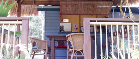 Un espacio al aire libre techado con piso de madera, dos sillas de mimbre, una mesa y un letrero de salida.
