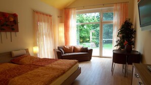 A bedroom with a large bed, a sofa, a TV, and a sliding glass door leading to a garden. - Badische Landoase (Kehl)