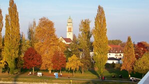 A riverside view with autumn trees, a church tower, and a pedestrian path. - Badische Landoase (Kehl)