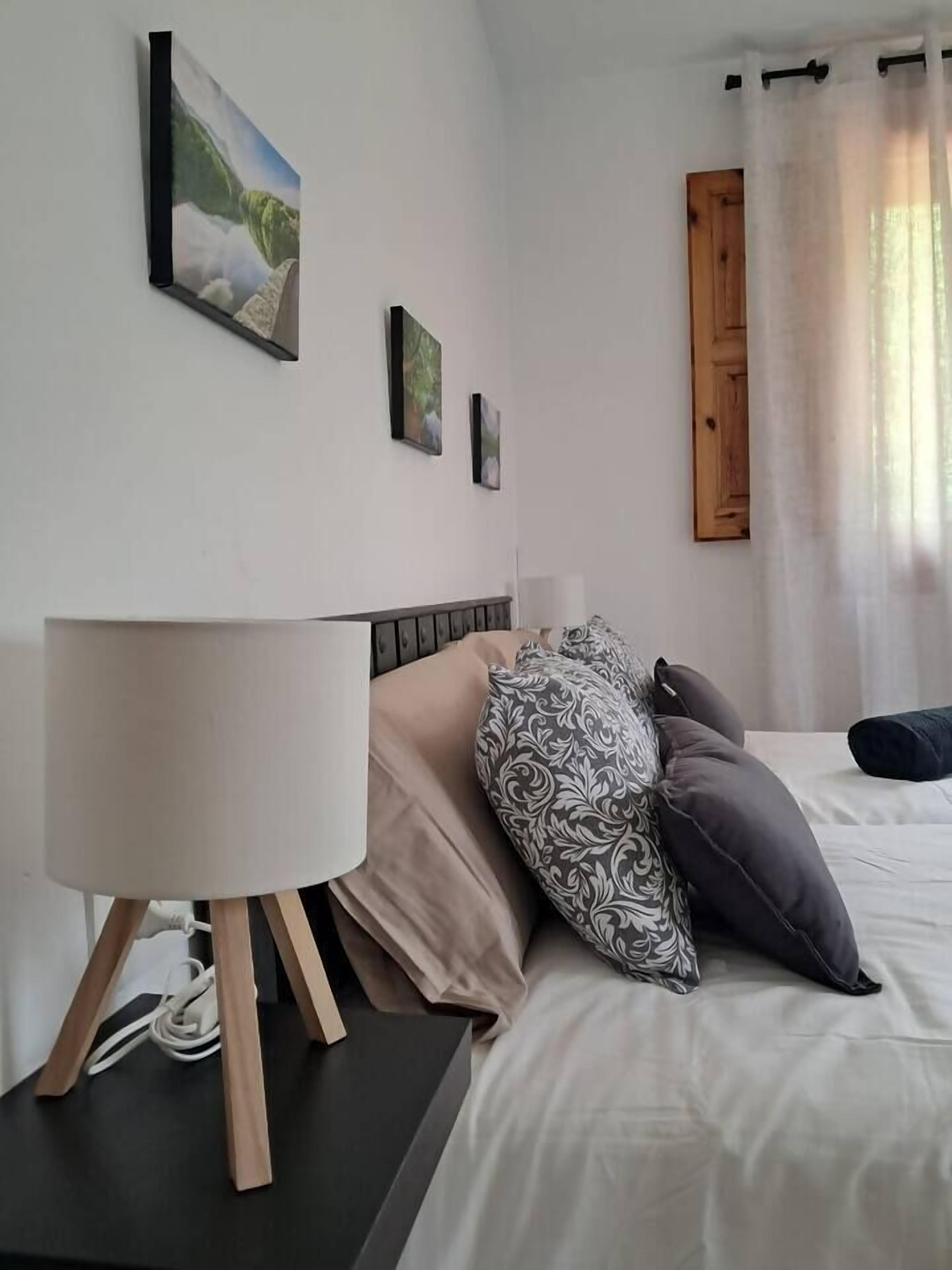 Un dormitorio con una cama, una mesita de noche con lámpara y dos cuadros colgados en la pared.