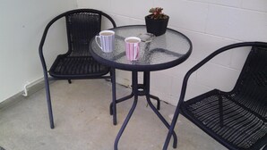 A small outdoor seating area with two chairs and a table, a potted plant, and two striped mugs. - Snowy River Lodge Motel (Newmerella)