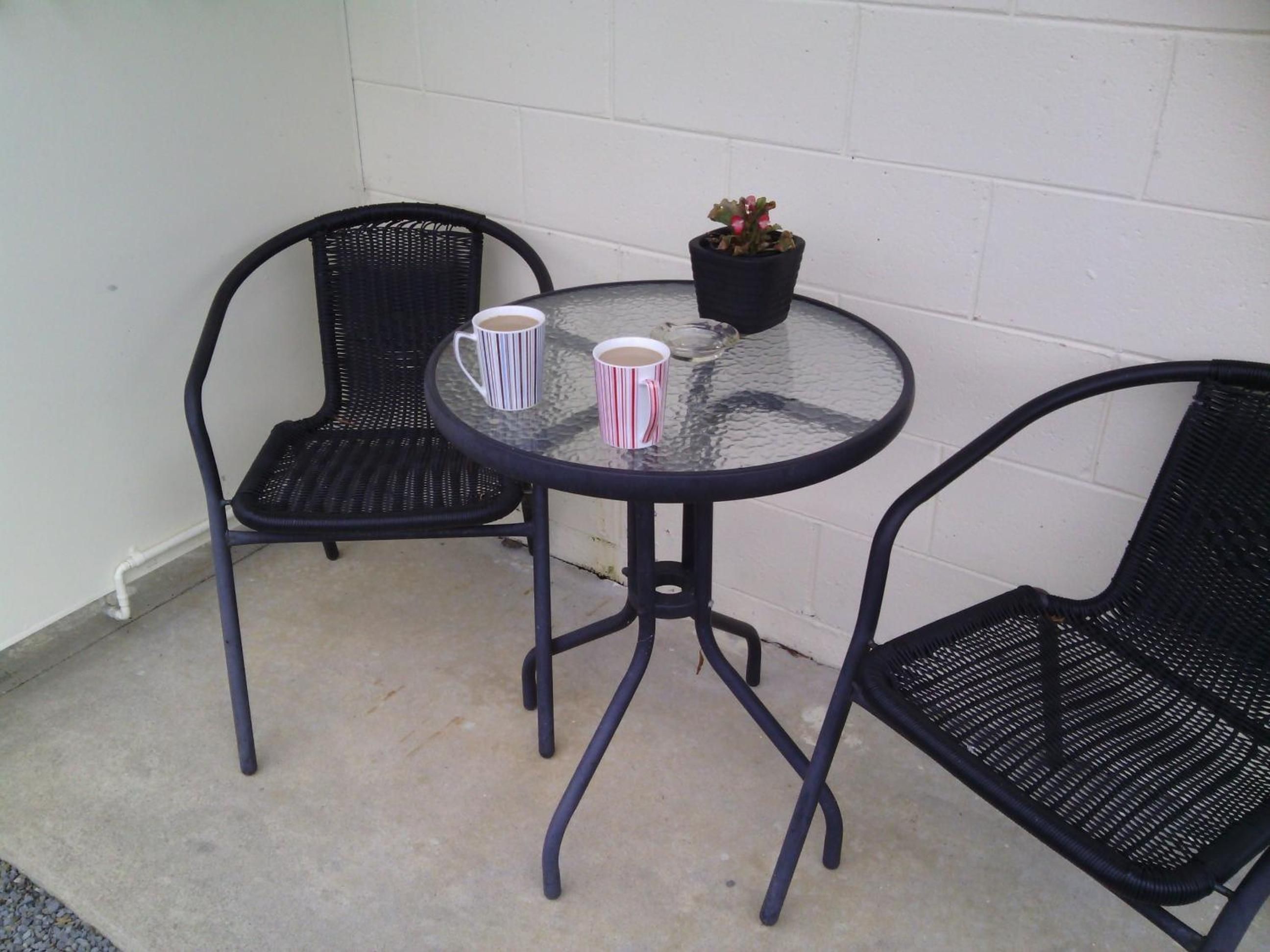 A small outdoor seating area with two chairs and a table, a potted plant, and two striped mugs.