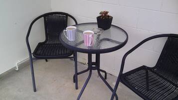 A small outdoor seating area with two chairs and a table, a potted plant, and two striped mugs.