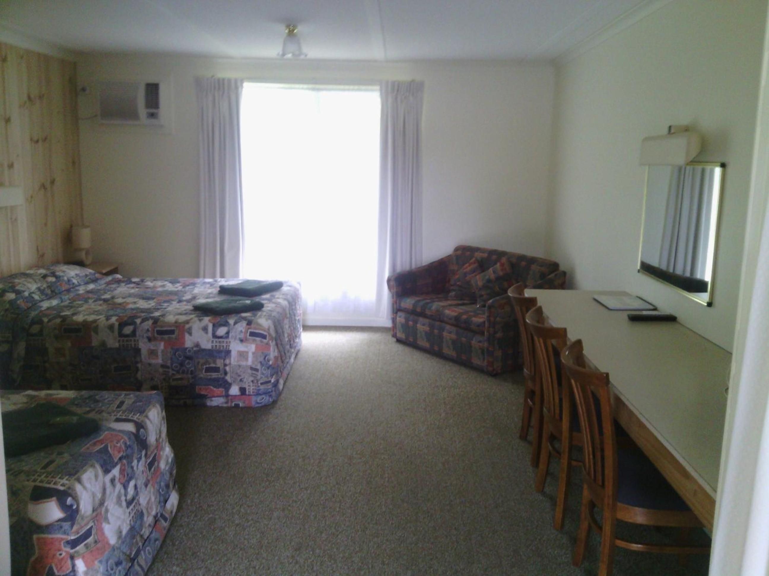 A hotel room with two beds, a sofa, a desk with a chair, and a large window.