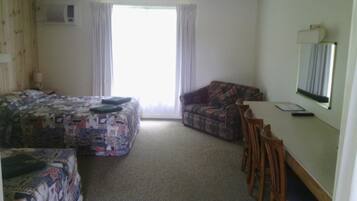 A hotel room with two beds, a sofa, a desk with a chair, and a large window.