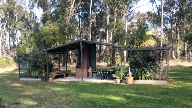 A covered outdoor area with a barbecue, seating, and potted plants. - Snowy River Lodge Motel (Newmerella)