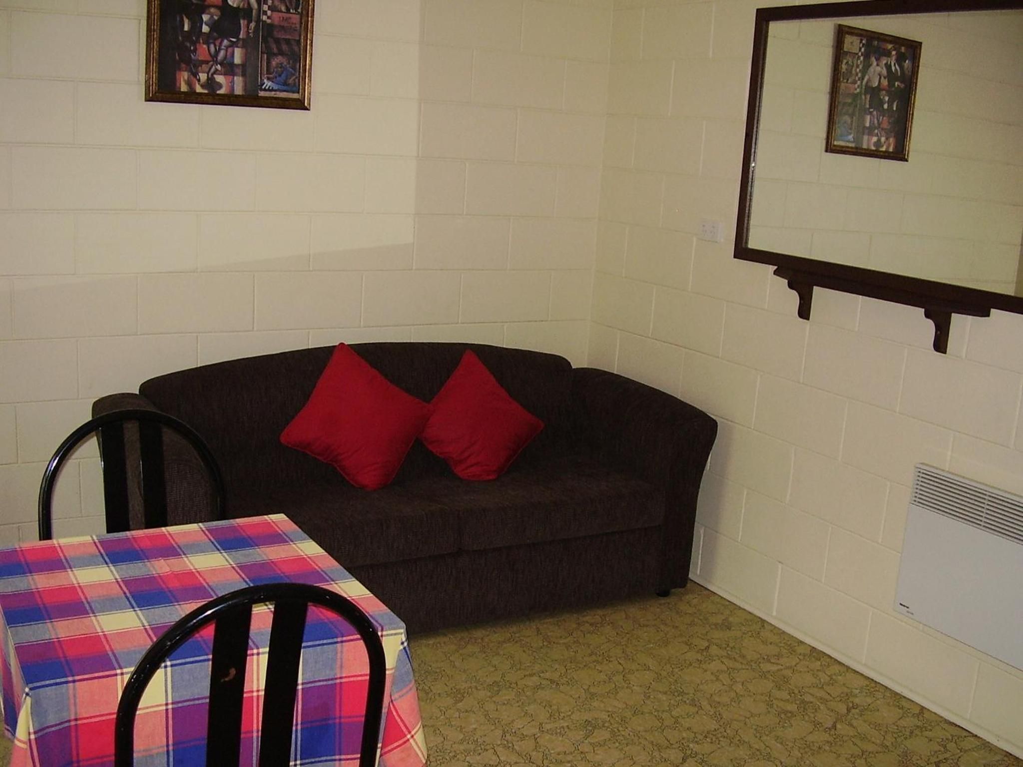 A room with a dark brown sofa, two red pillows, a plaid table, and a chair.