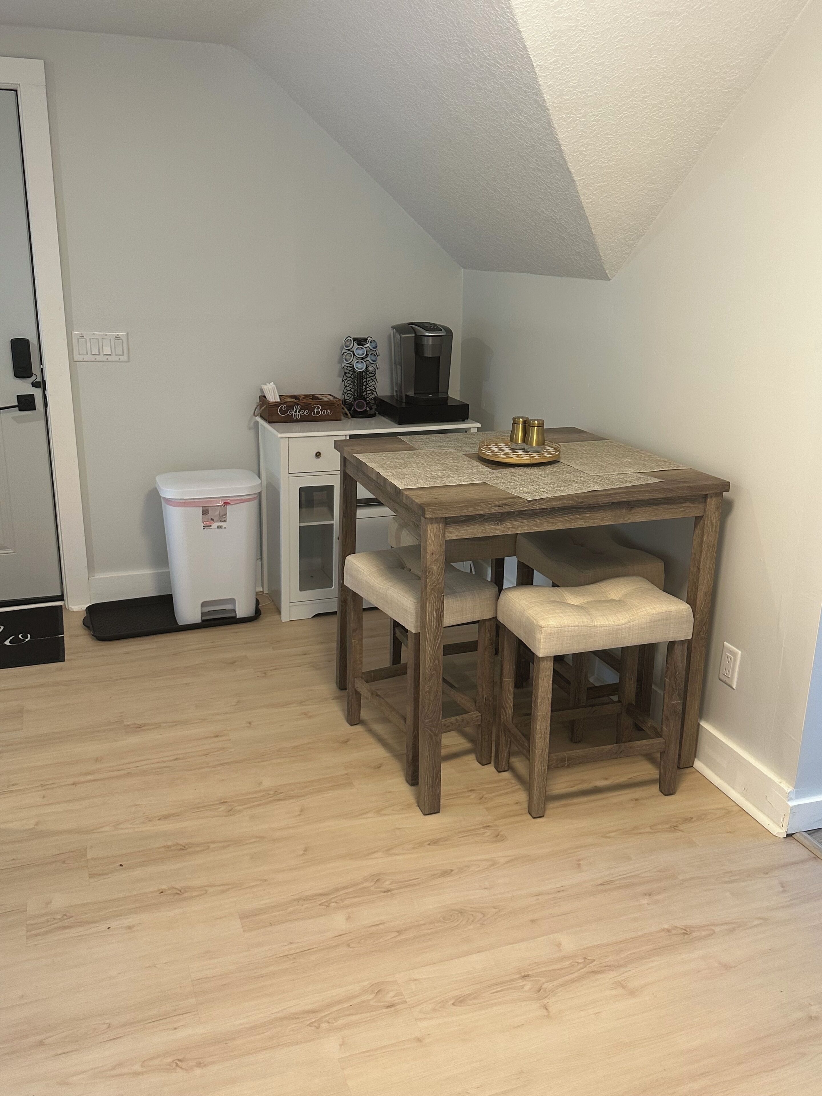En matplats med ett träbord och en träbänk, en kaffebryggare och en papperskorg.