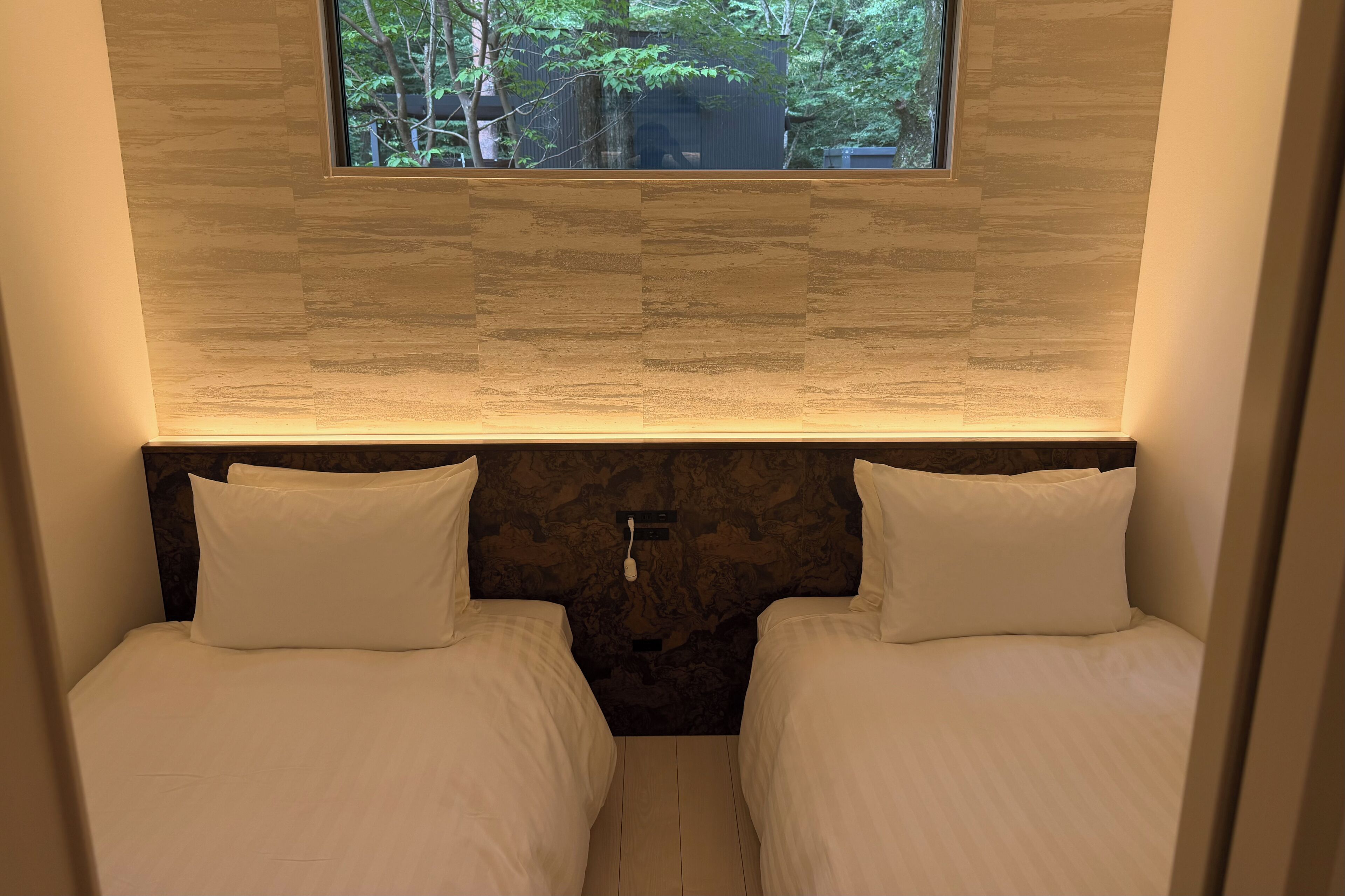 Una habitación pequeña y acogedora con dos camas, una ventana y una pared con textura.