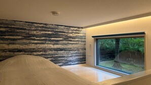 Een kamer met een groot raam, een plafondlamp en een structuurwand.