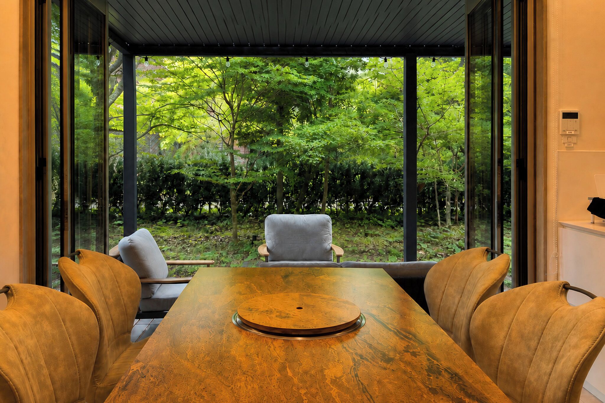 A dining area with a wooden table and two chairs, large windows offering a view of a garden.