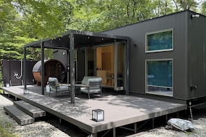 A modern outdoor deck with seating, a covered area, and a large window. - Mori no Rikyu (Sunto-gun)
