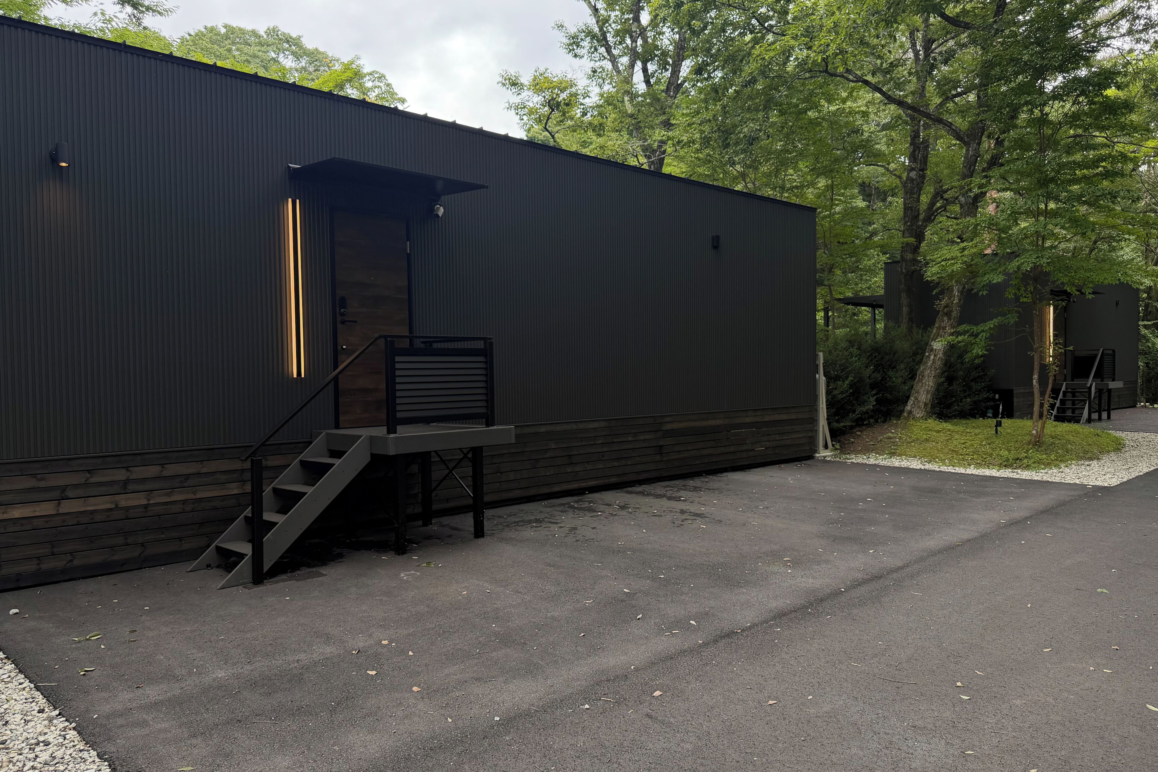 A modern building with a dark exterior, a wooden deck, and a staircase leading to an entrance.