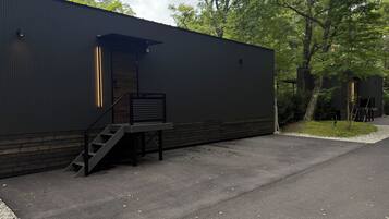 A modern building with a dark exterior, a wooden deck, and a staircase leading to an entrance.