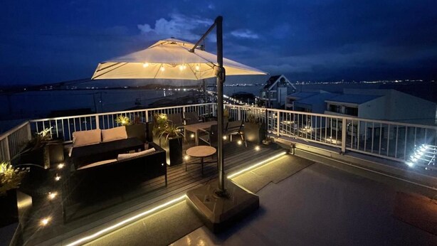 Een dakterras met buitenmeubilair, een grote parasol en een uitzicht op de skyline van de stad in de avond.