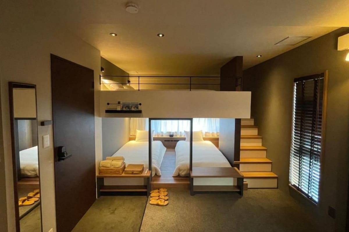 A hotel room with a bunk bed, a desk, and a window with blinds.