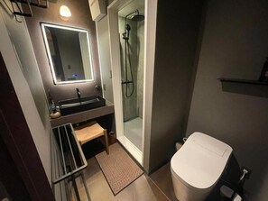 A modern bathroom with a glass-enclosed shower, a white toilet, and a vanity with a mirror. - HITOYOI SENRI Rooftop BBQ Ocean View (Fukuoka)