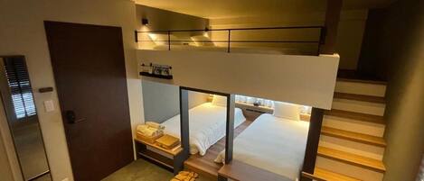 A hotel room with a bunk bed, a desk, a chair, and a small table.